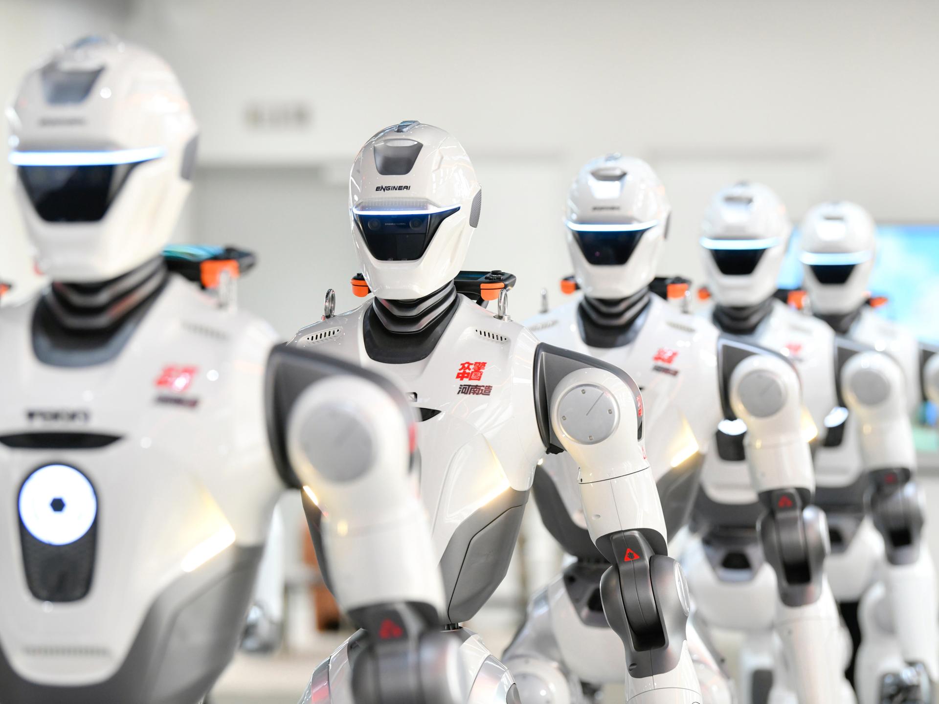 Mehrere humanoide Roboter der chinesischen Firma EngineAI stehen in einer Reihe. Mehrere humanoide Roboter der chinesischen Firma EngineAI stehen in einer Reihe.