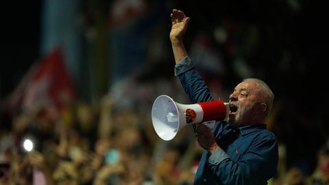 Lula da Silva hält ein Megafon vor den Mund und ruft hinein, die andere Hand hat er hoch erhoben. 