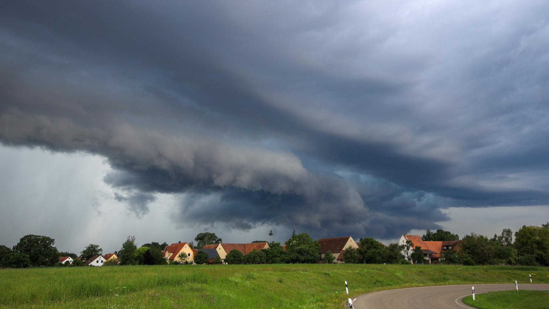 Das Bild zeigt einige Häuser eines Ortes. Am Himmel bilden sich dunkle Wolkenfronten.