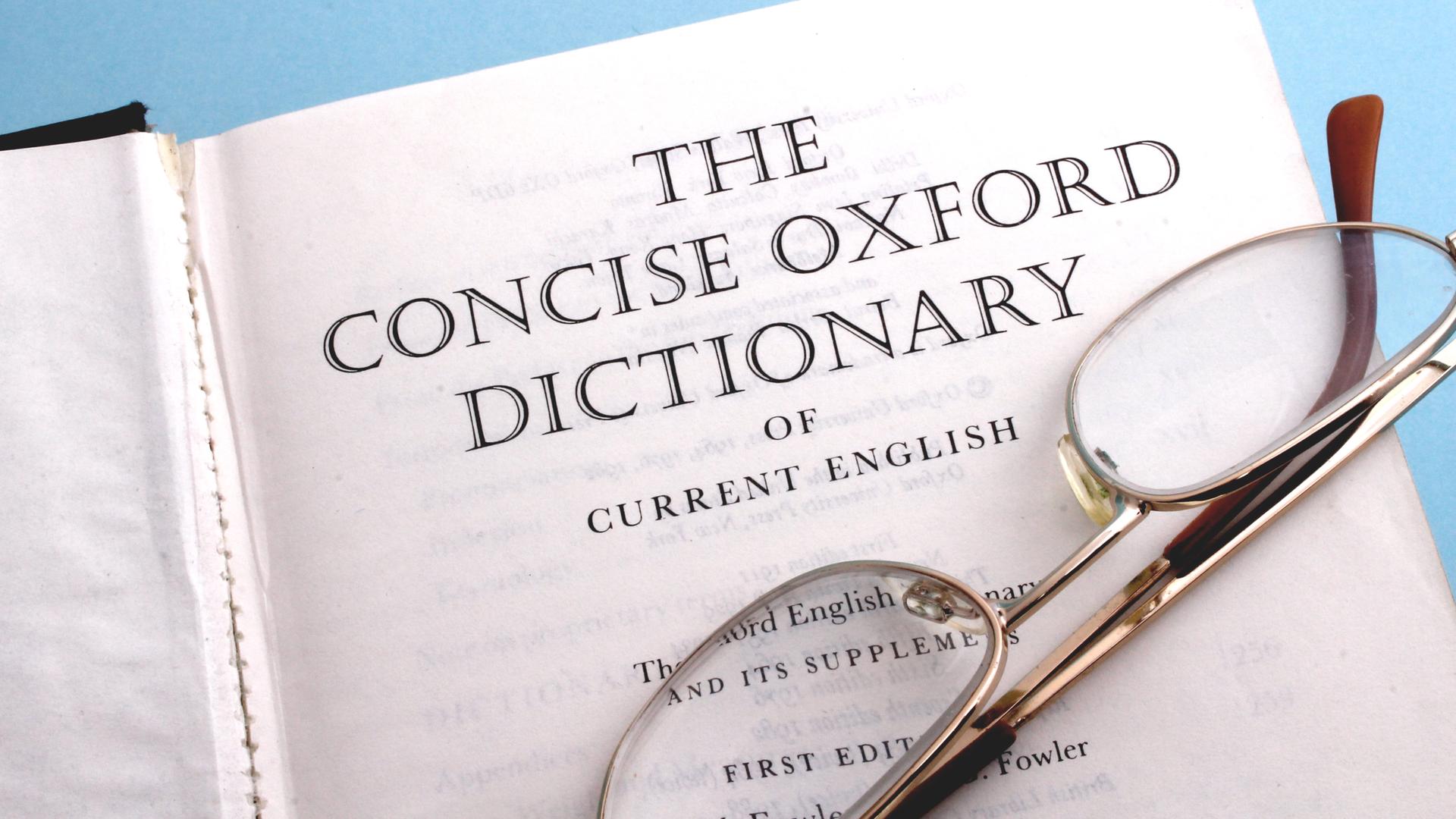 Ein Exemplar des Oxford Dictionary liegt aufgeschlagen auf der Titelseite und darauf liegt noch eine zusammengefaltete Brille.