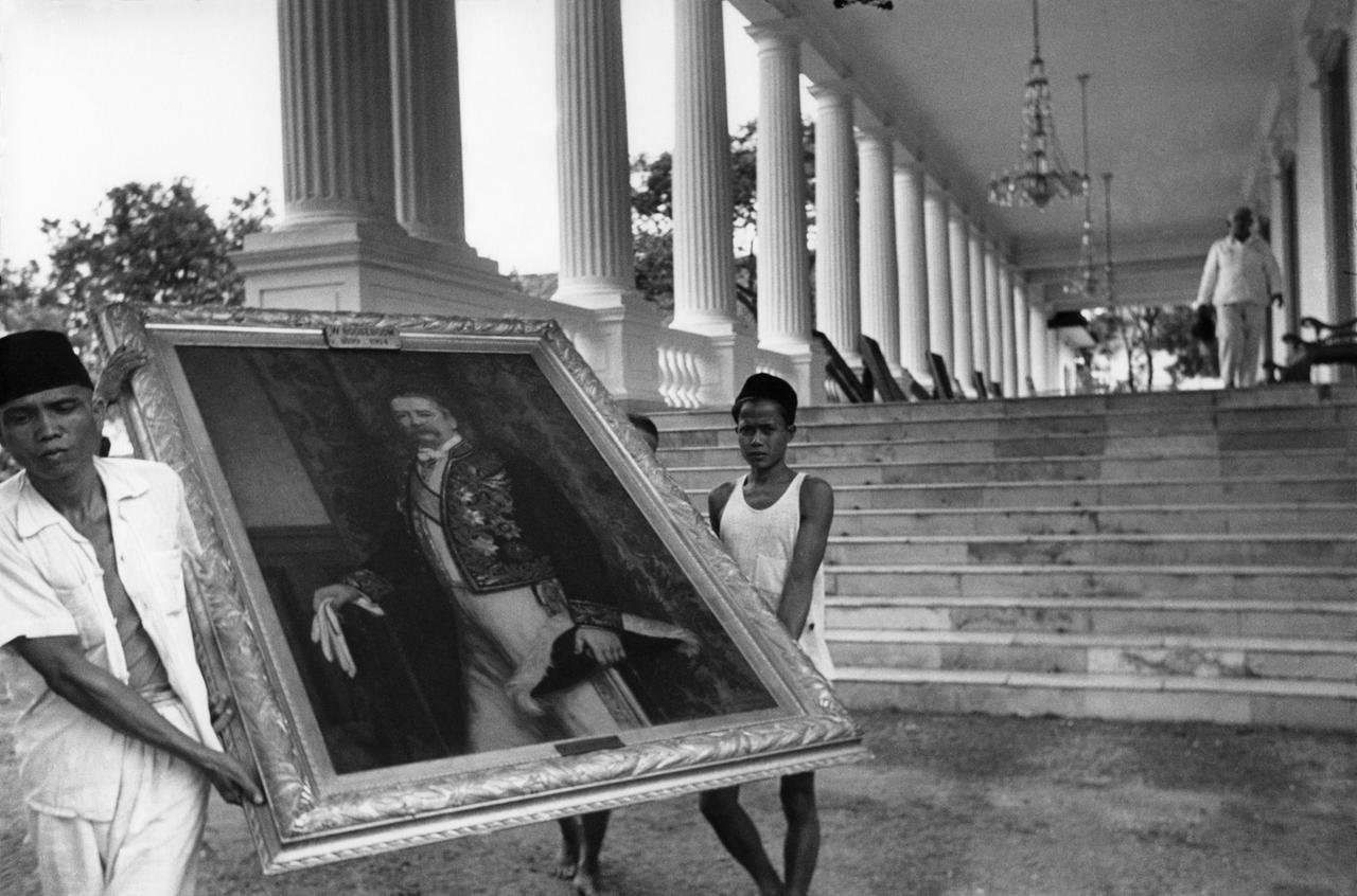 Zwei Indonesier tragen ein Ölgemälde eines niederländischen Gouverneurs aus einem Palast.