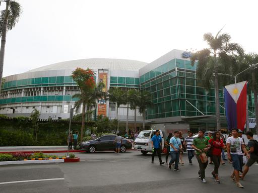 Menschen überqueren die Straße vor dem Araneta Coliseum in einem Vorort der Stadt Quezon, nordöstlich von Manila gelegen. Der "Big Dome" war vor fast 50 Jahren  der Austragungsort des epischen Schwergewichts-Boxkampfs "Thrilla in Manila" zwischen Muhammad Ali und Joe Frazier im Jahr 1975, den Ali durch einen technischen K.O. in der 15. Runde gewann.