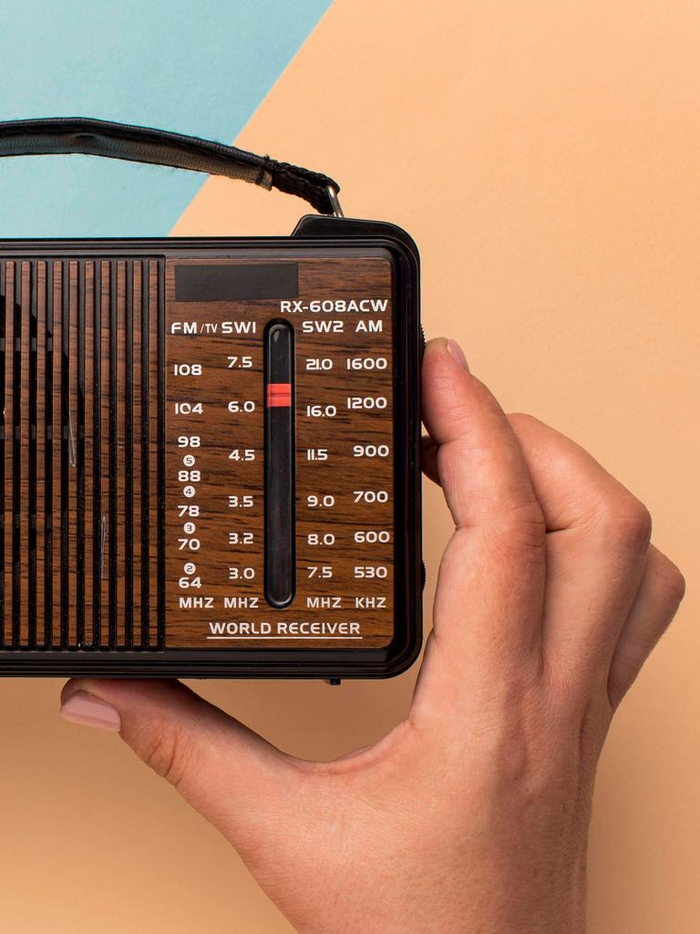 Hände halten ein kleines Retro-Radio vor einem farbigem Hintergrund aus geometrischen Formen. 