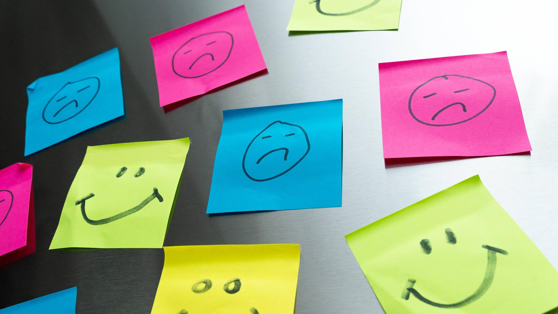 Bunte Post-its mit glücklichen und traurigen Gesichtern Bunte Post-its mit glücklichen und traurigen Gesichtern