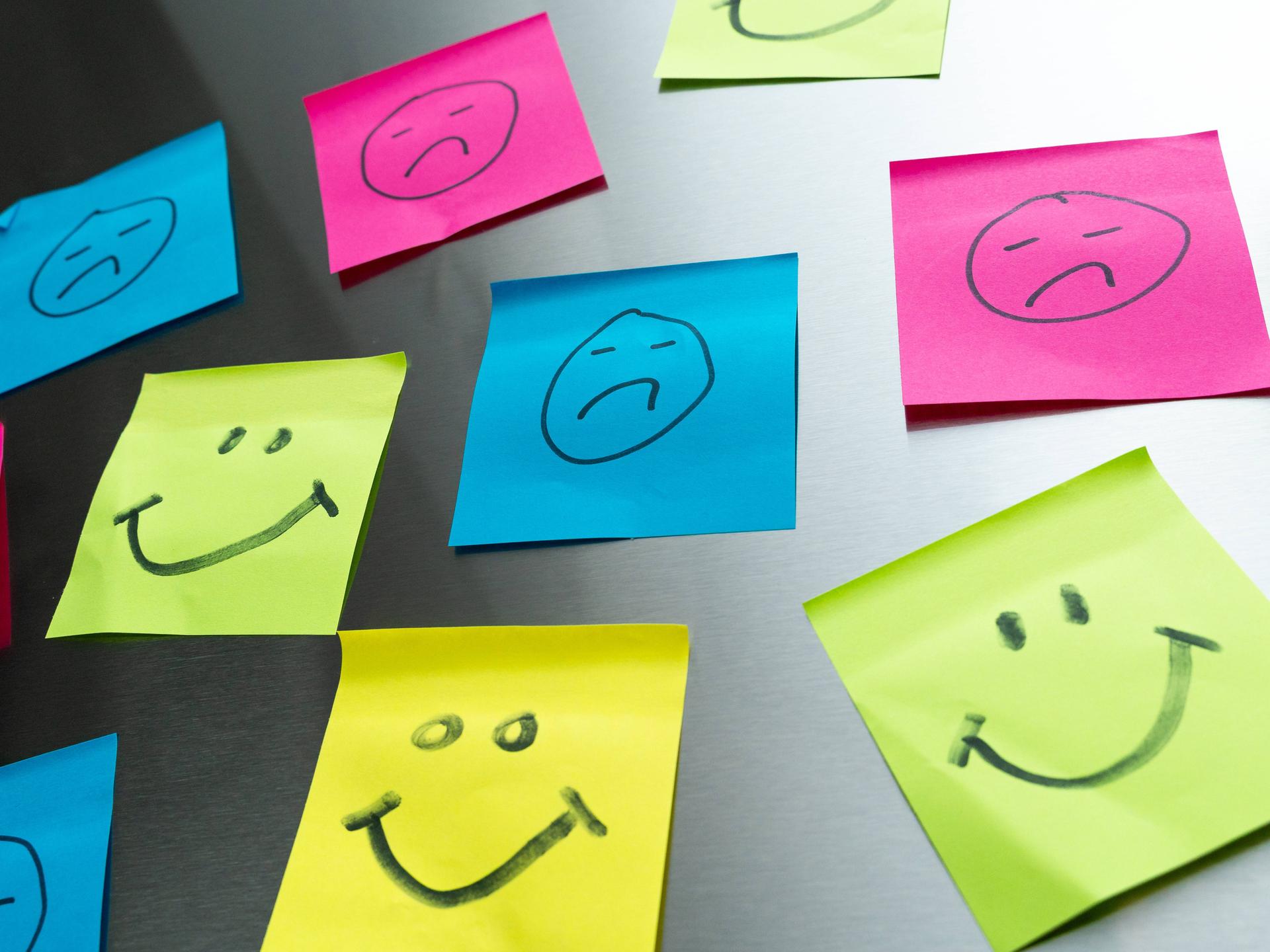 Bunte Post-its mit glücklichen und traurigen Gesichtern