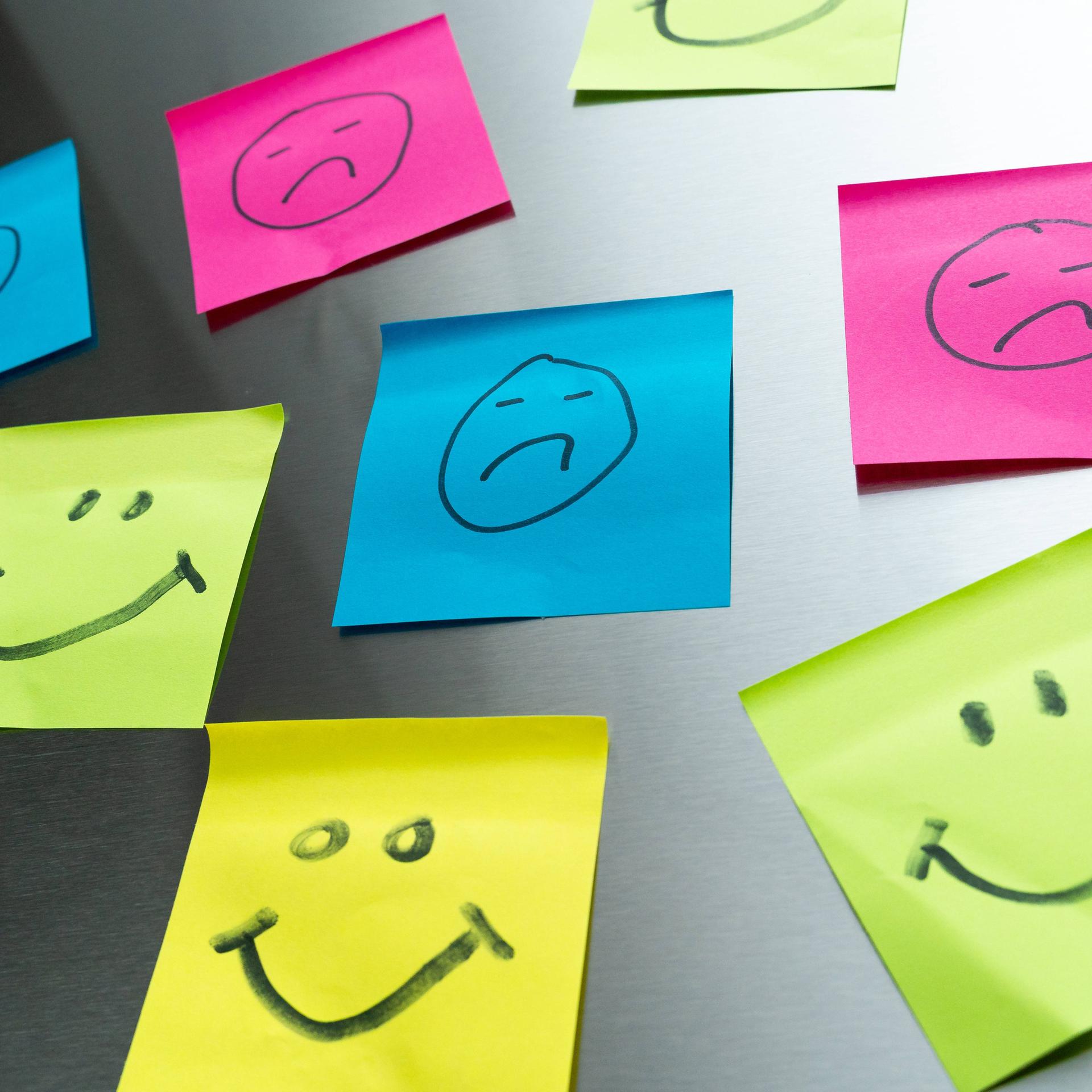 Bunte Post-it mit glücklichen und traurigen Gesichtern.