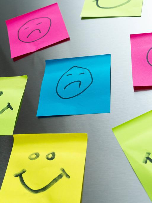 Bunte Post-its mit glücklichen und traurigen Gesichtern Bunte Post-its mit glücklichen und traurigen Gesichtern