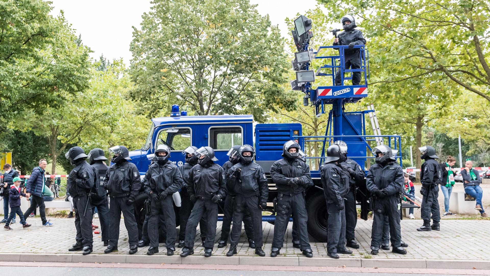 Zahlreiche Polizisten in Schutzuniform stehen vor einem Einsatzfahrzeug. Auf einem erhöhten Podesz steht ein Beamter mit Kamera.