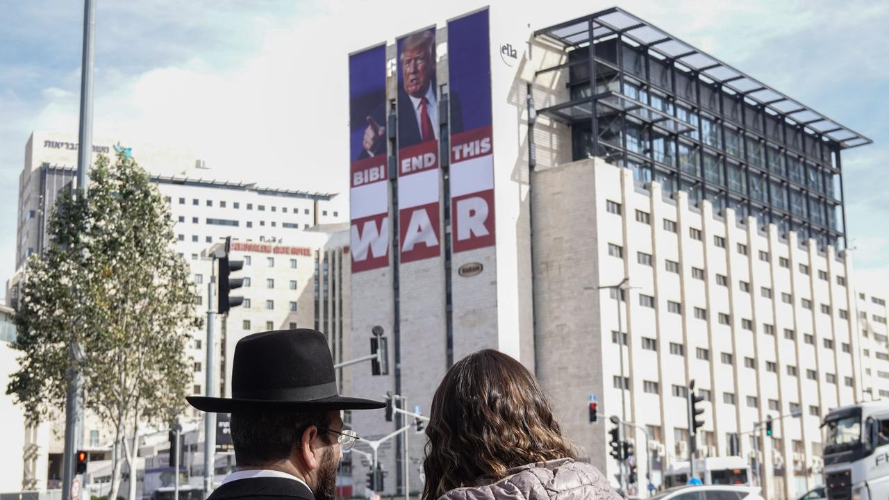 An einer Hauswand in Jerusalem hängt ein großes Plakat mit einem Bild von Donald Trump und dem Slogan: "Bibi end this war" (Bibi, beende diesen Krieg.) Bibi ist der Spitzname von Premierminister Netanyahu. Es ist eine Straßenszene mit zwei Menschen.