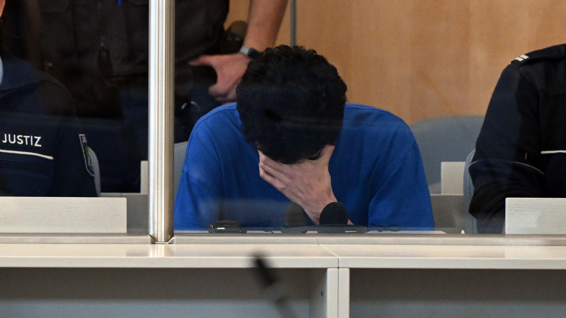 Der Angeklagte im Gerichtssaal der Oberlandesgerichts mit gesenktem Kopf und einer Hand vor dem Gesicht