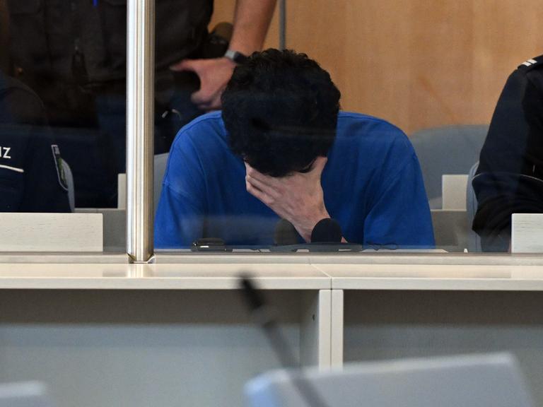 Der Angeklagte im Gerichtssaal der Oberlandesgerichts mit gesenktem Kopf und einer Hand vor dem Gesicht