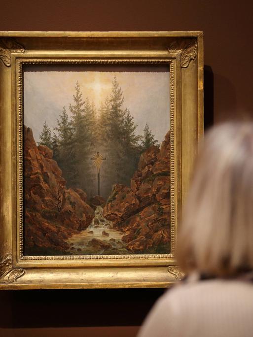 Eine Frau betrachtet das Gemälde "Kreuz im Wald" von Caspar David Friedrich (um 1812) in einer Ausstellung.