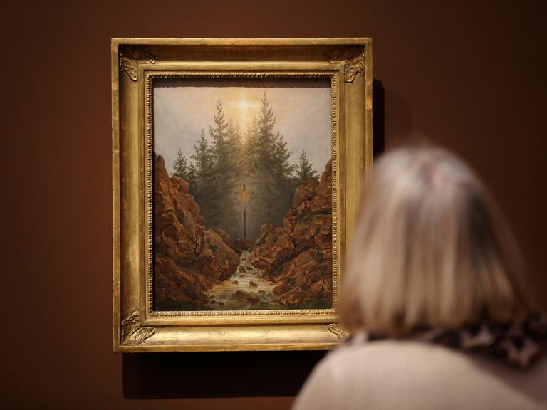 Eine Frau betrachtet das Gemälde "Kreuz im Wald" von Caspar David Friedrich (um 1812) in einer Ausstellung.