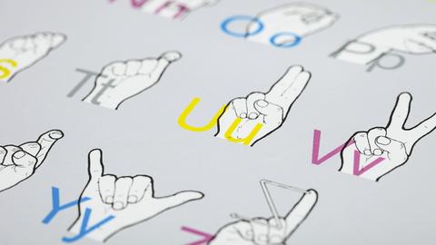 Eine Tafel zum Lernen der Gebärdensprache zeigt bunte Buchstaben und die dazugehörigen Handzeichen.