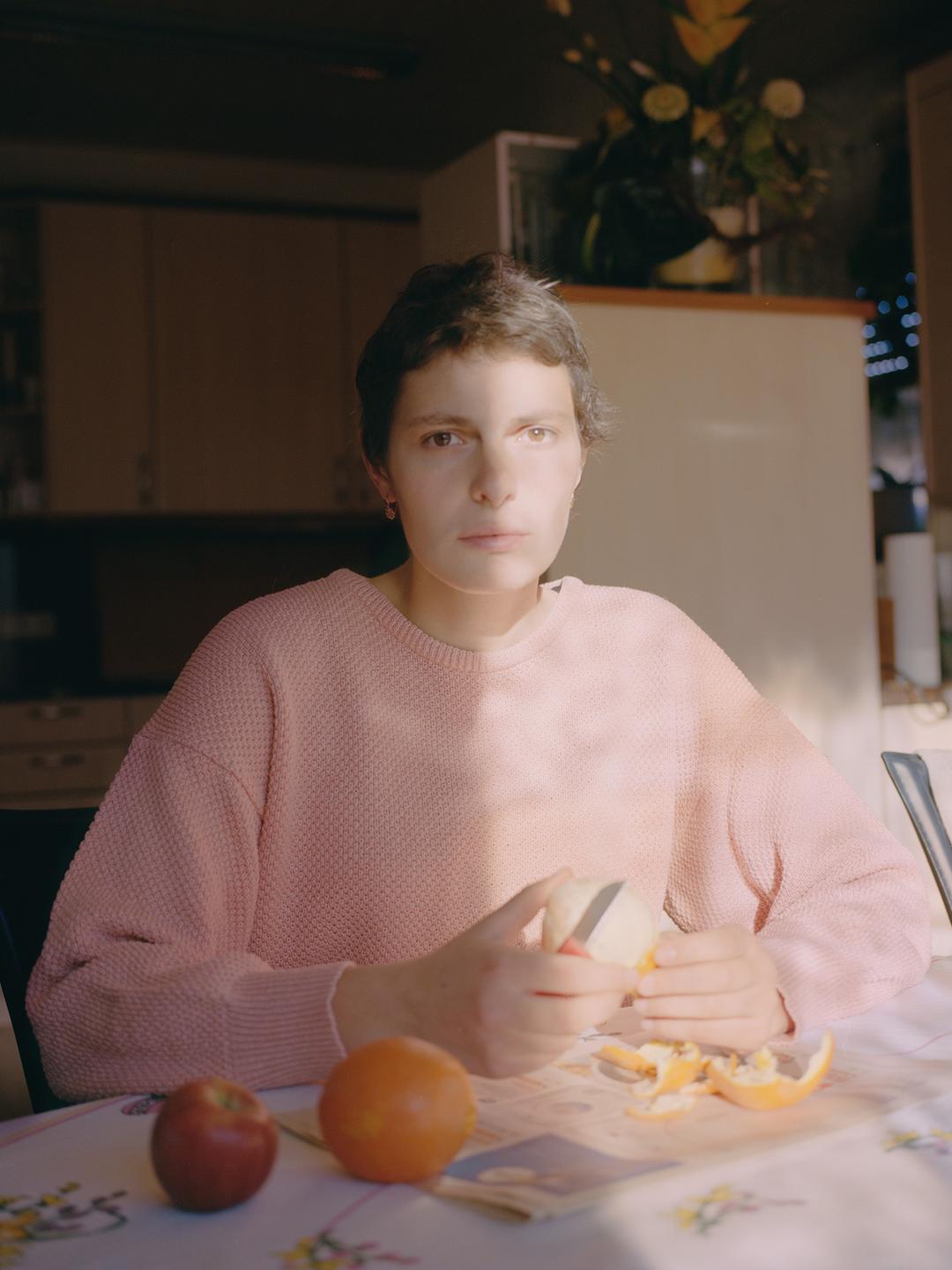 Die Fotografin Mika Sperling sitzt an einem Tisch mit Orangen. Sie trägt einen pastellfarbenen Strickpullover.