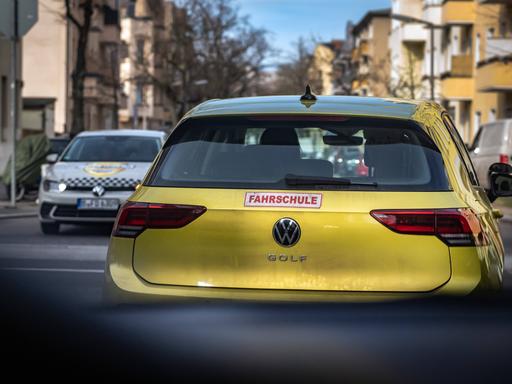 Blick durch die Frontscheibe eines PKW auf ein Auto mit der Aufschrift "Fahrschule" am Heck.