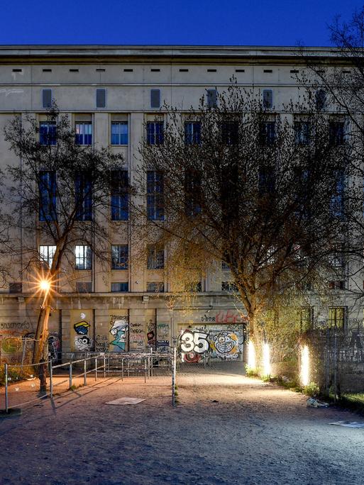 Der Eingangsbereich zum Club Berghain: ein rechteckiges Industriegebäude mit Fassade, unterbrochen von vertikalen Fensterflächen, davor mehrere Lampen zur Beleuchtung
