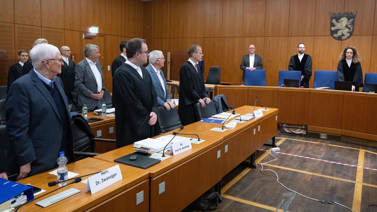 Angeklagte, Anwälte und Richter erheben sich in einem Prozesssaal.