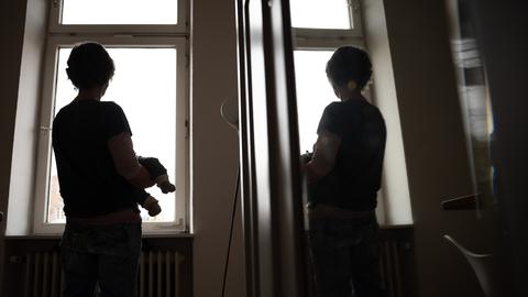 Eine Frau hält ein Kleinkind auf dem Arm während sie sich in einer Spiegeltür spiegelt.