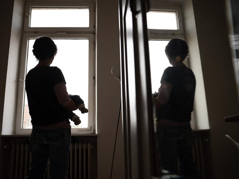 Eine Frau hält ein Kleinkind auf dem Arm während sie sich in einer Spiegeltür spiegelt.