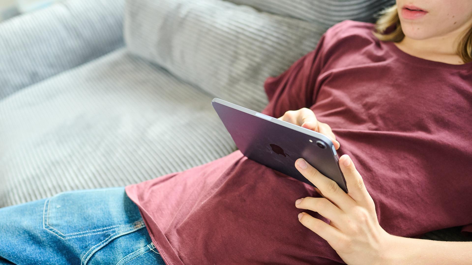 Ein Teenager liegt auf einer Couch und guckt auf ein iPad Ein Teenager liegt auf einer Couch und guckt auf ein iPad