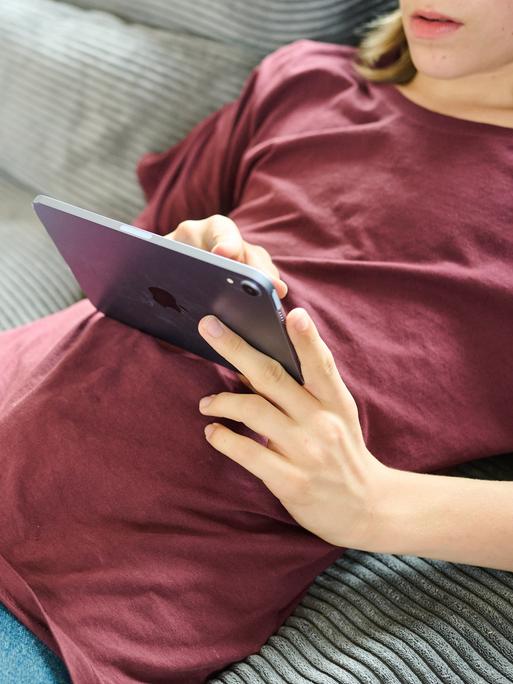 Ein Teenager liegt auf einer Couch und guckt auf ein iPad