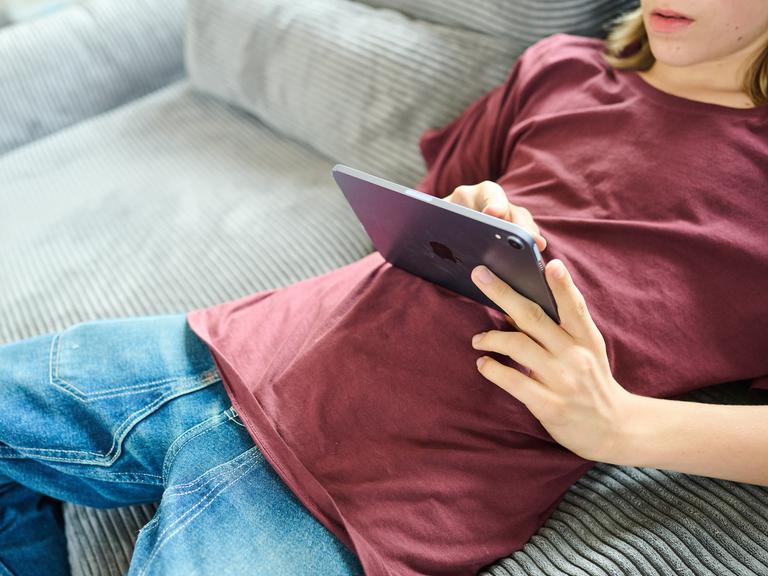 Ein Teenager liegt auf einer Couch und guckt auf ein iPad