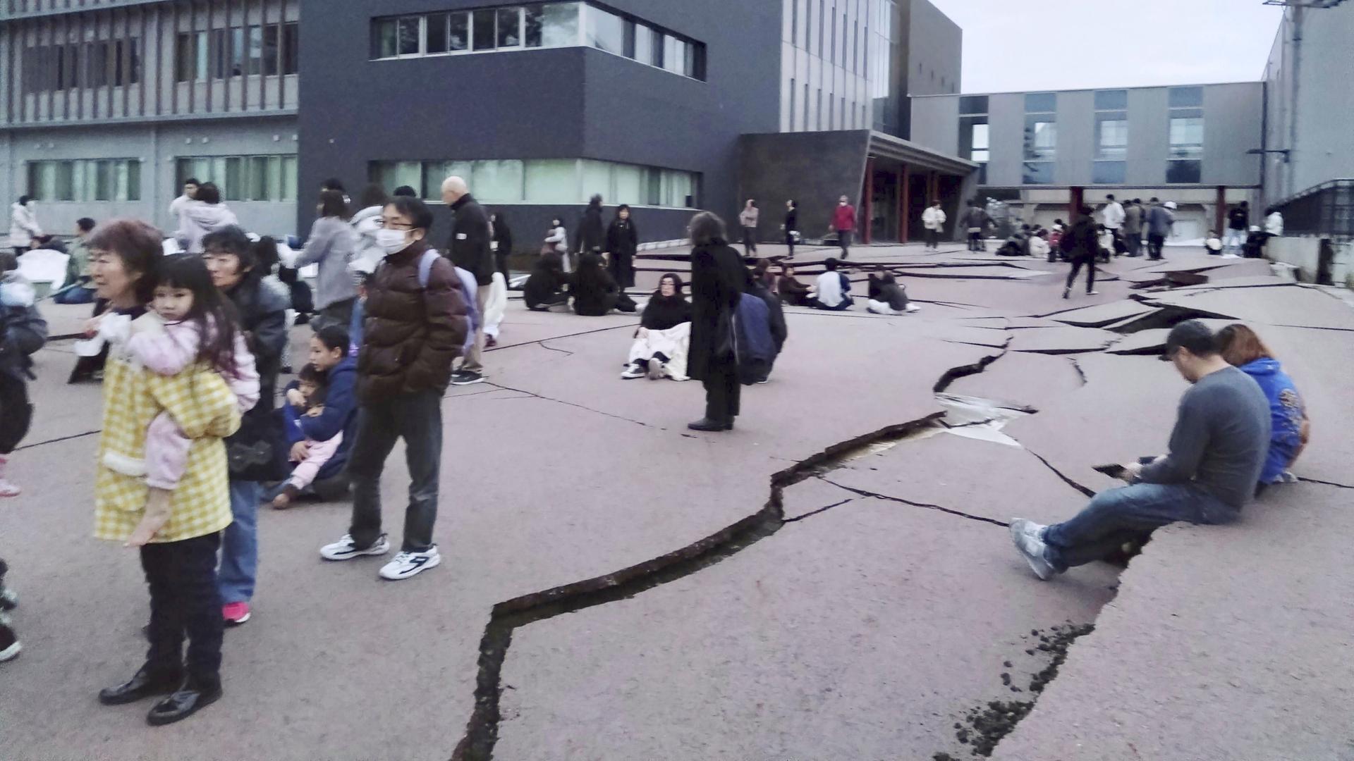In Wajima, Präfektur Ishikawa sind nach einem Erdbeben Risse im Boden zu sehen. Mehrere Passanten stehen oder sitzen daneben. In Wajima, Präfektur Ishikawa sind nach einem Erdbeben Risse im Boden zu sehen. Mehrere Passanten stehen oder sitzen daneben.