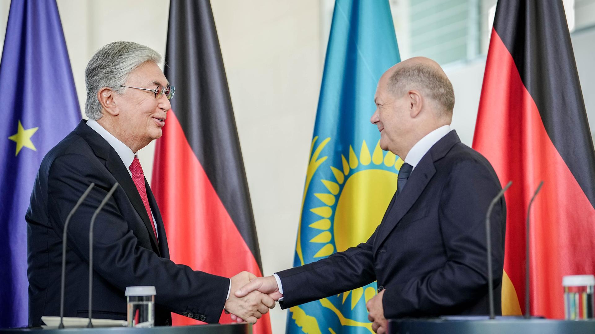 Bundeskanzler Olaf Scholz und der kassachische Präsident Kassim-Schomart Tokajew geben sich während einer Pressekonferenz die Hand, im Hintergrund sind die Flaggen Deutschlands, Kasachstans und der EU aufgestellt.