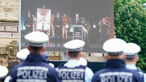 Polizisten stehen bei einer Trauerfeier in Mannheim für vor einer Leinwand, die die Bühne eines Veranstaltungszentrums zeigt. 