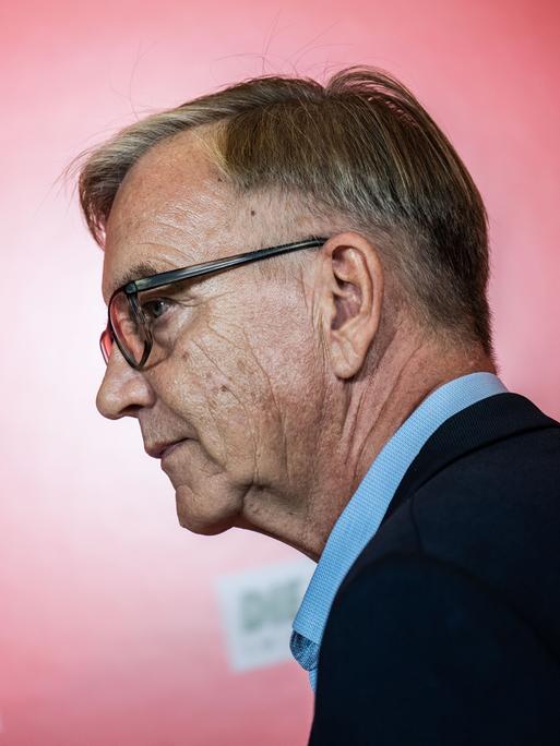 Dietmar Bartsch, Fraktionsvorsitzender der Partei Die Linke, von der Seite fotografiert, vor rotem Hintergrund.