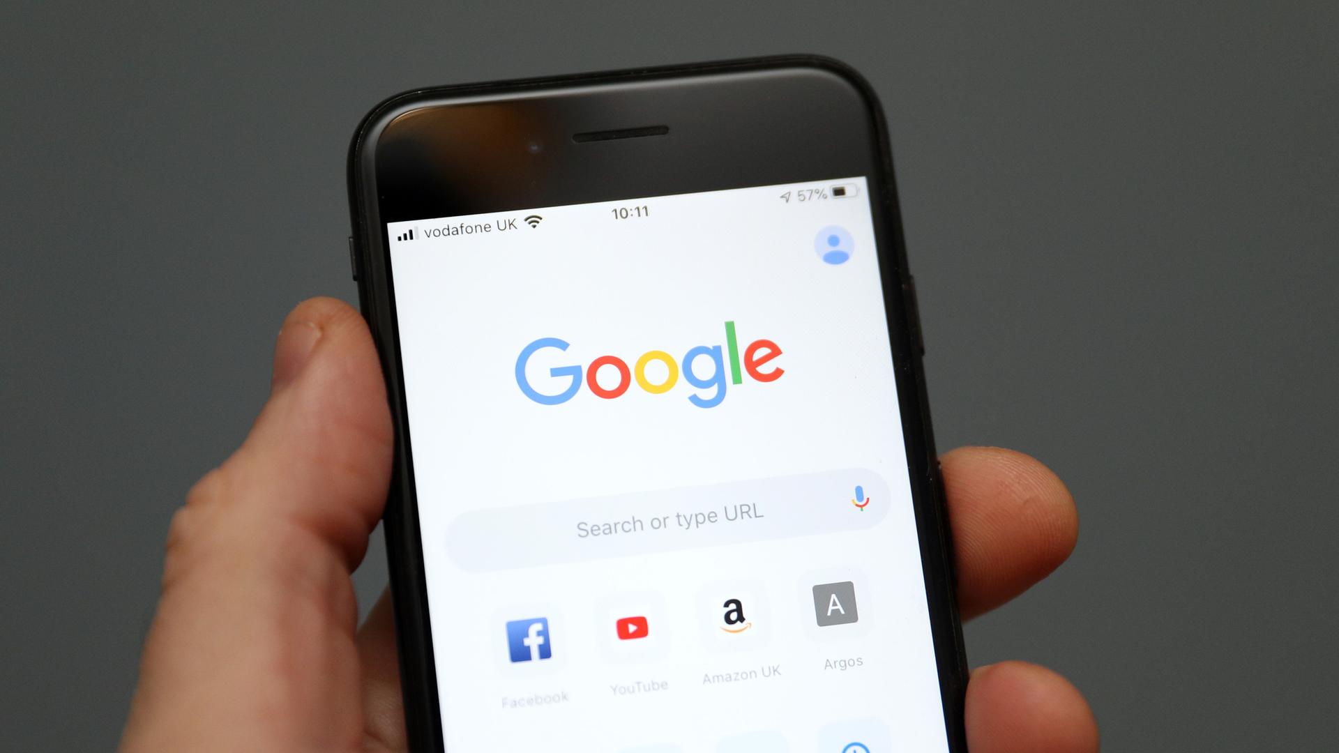 Eine Hand hält ein Mobiltelefon auf dessen Display die Oberfläche der Suchmaschine Google zu sehen ist. 