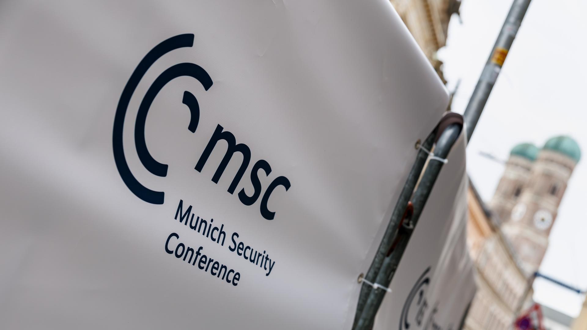 An einem Absperrgitter vor dem Bayerischen Hof ist die Aufschrift „MSC - Munich Security Conference“ zu sehen, im Hintergrund die Münchner Frauenkirche.