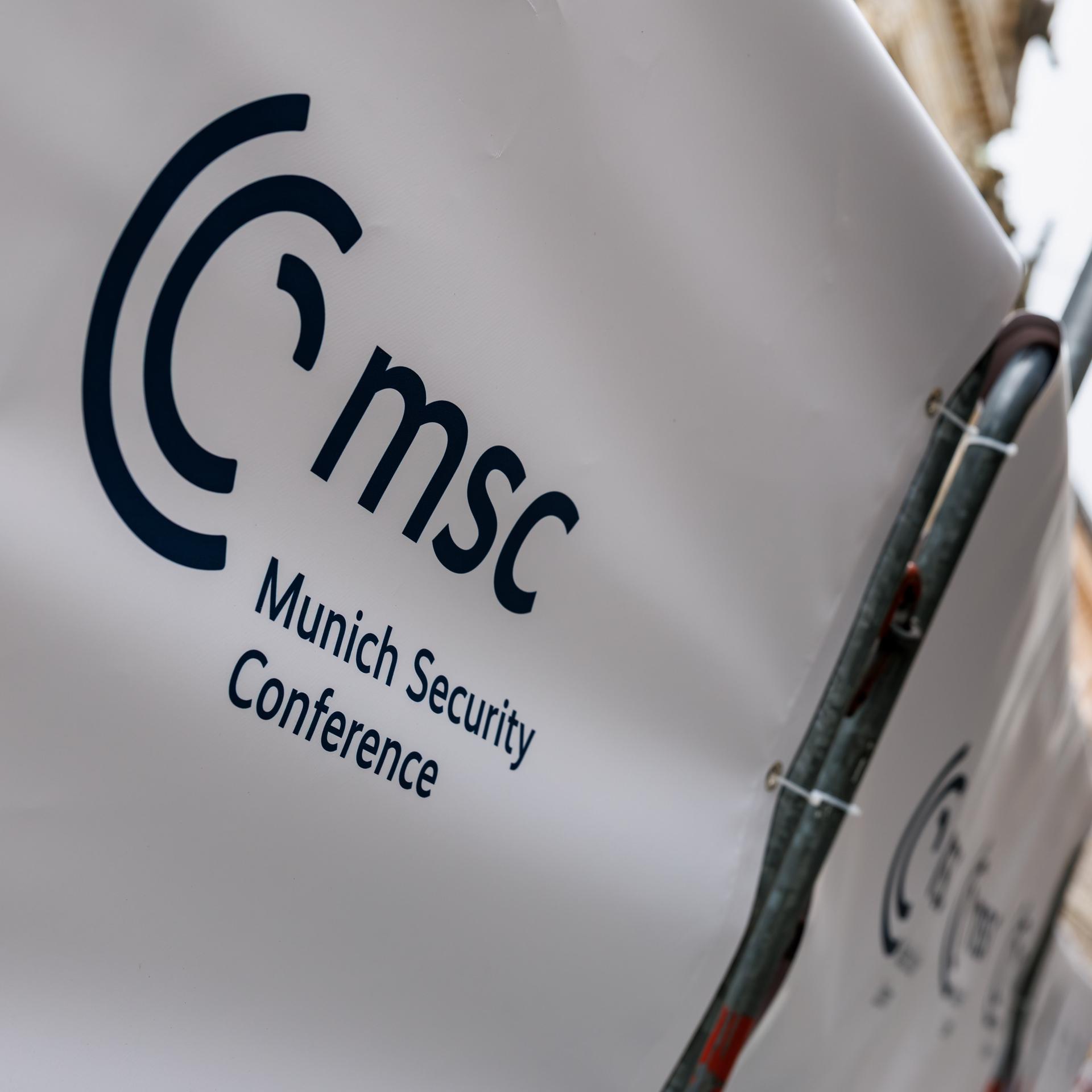 An einem Absperrgitter vor dem Bayerischen Hof ist die Aufschrift „MSC - Munich Security Conference“ zu sehen, im Hintergrund die Münchner Frauenkirche.