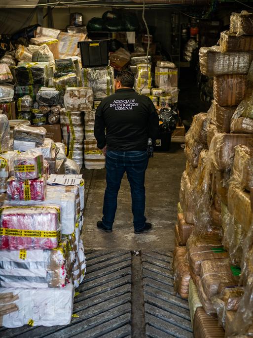 Ein mexikanischer Kriminalbeamter steht inmitten eines Lagers mit beschlagnahmtem Fentanyl und Meth in folienumwickelten Paketen.