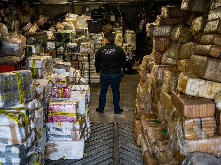 Ein mexikanischer Kriminalbeamter steht inmitten eines Lagers mit beschlagnahmtem Fentanyl und Meth in folienumwickelten Paketen.