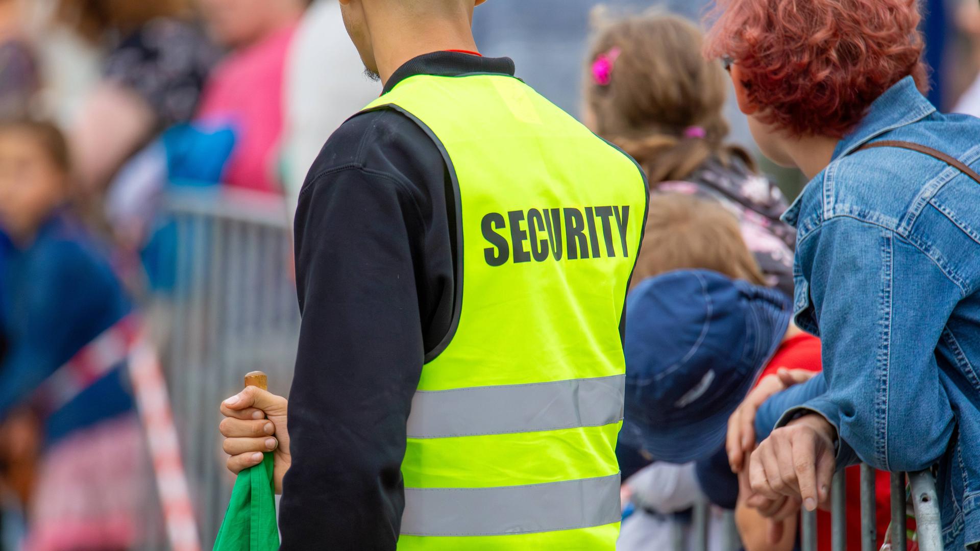 Mitarbeiter eines Sicherheitsdienstes mit gelber Warnweste mit Aufschrift "Security" sichert eine Veranstaltung.