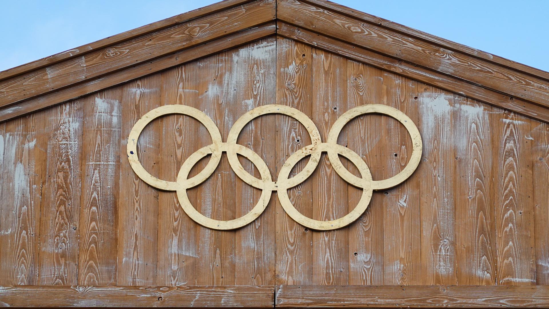 Die Olympischen Ringe hängen an einer Holzfassade