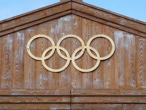 Die Olympischen Ringe hängen an einer Holzfassade