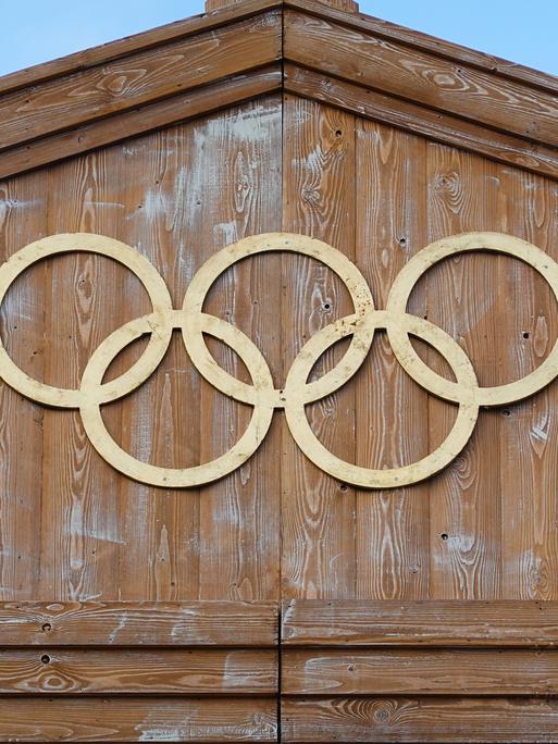 Die Olympischen Ringe hängen an einer Holzfassade