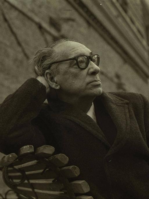 Juan Carlos Onetti sitzt auf einer Bank, den Kopf auf einer Hand aufgestützt, und schaut nachdenklich in die ferne.