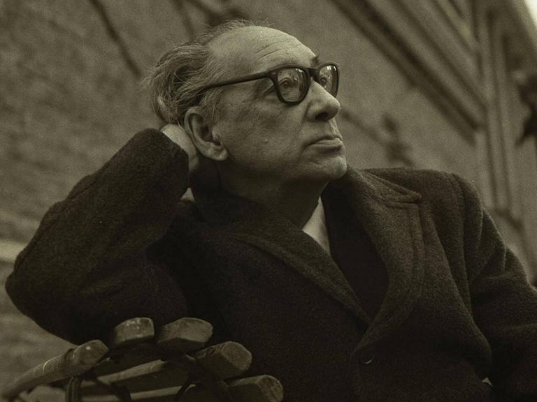 Juan Carlos Onetti sitzt auf einer Bank, den Kopf auf einer Hand aufgestützt, und schaut nachdenklich in die ferne.