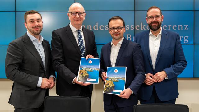 Politiker von SPD und CDU stehen zusammen und zeigen den neuen Koalitions-Vertrag. 