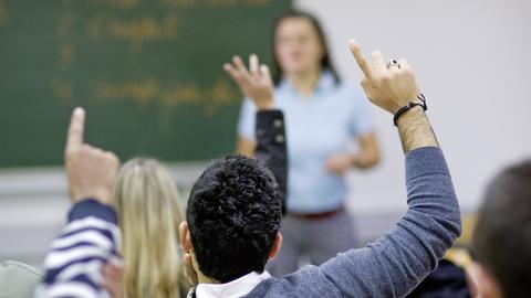Gymnasiasten der Oberstufe in einer Klasse beim Unterricht - Schüler melden sich beim Lehrer mit erhobenen Händen.