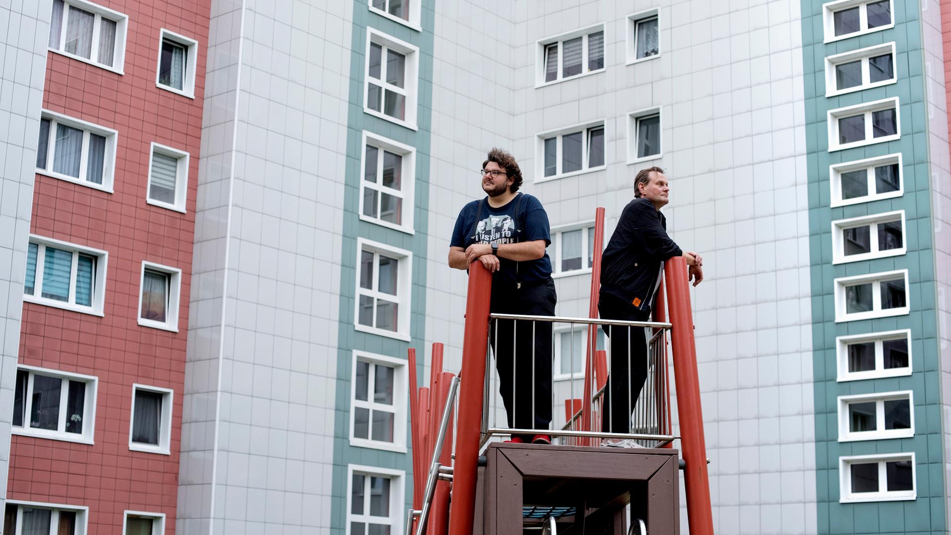 Devid Striesow und Axel Ranisch stehen auf einem Klettergerüst vor einer Plattenbaufassade und schauen in unterschiedliche Richtungen. Devid Striesow und Axel Ranisch stehen auf einem Klettergerüst vor einer Plattenbaufassade und schauen in unterschiedliche Richtungen.
