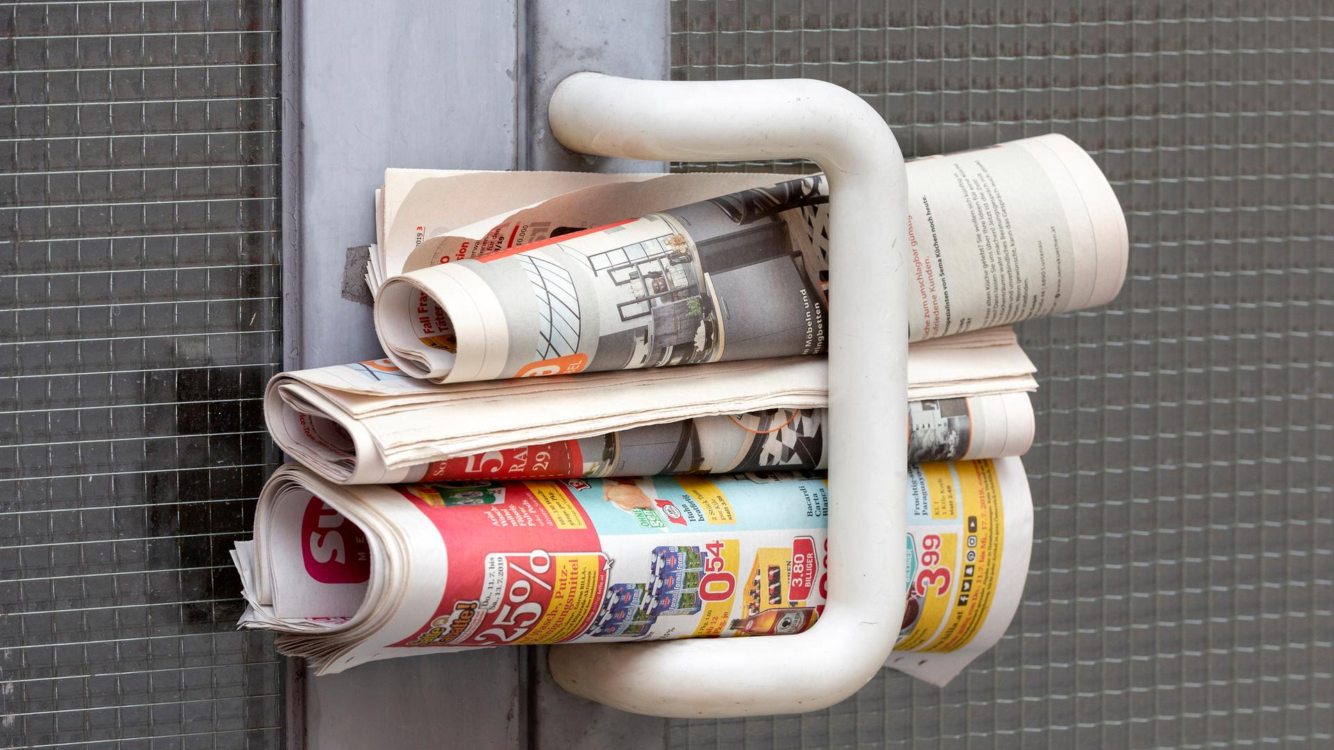Gratiszeitungen eingerollt an einem Türgriff einer Haustür
