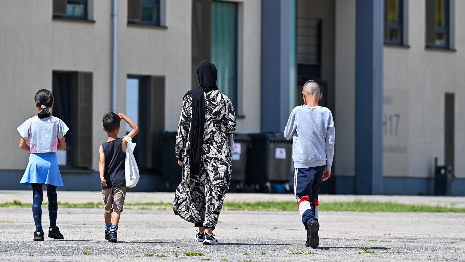 Eine Migrantin und ihre drei Kinder gehen über das Gelände der Erstaufnahmeeinrichtung. Sie sind von hinten zu sehen.