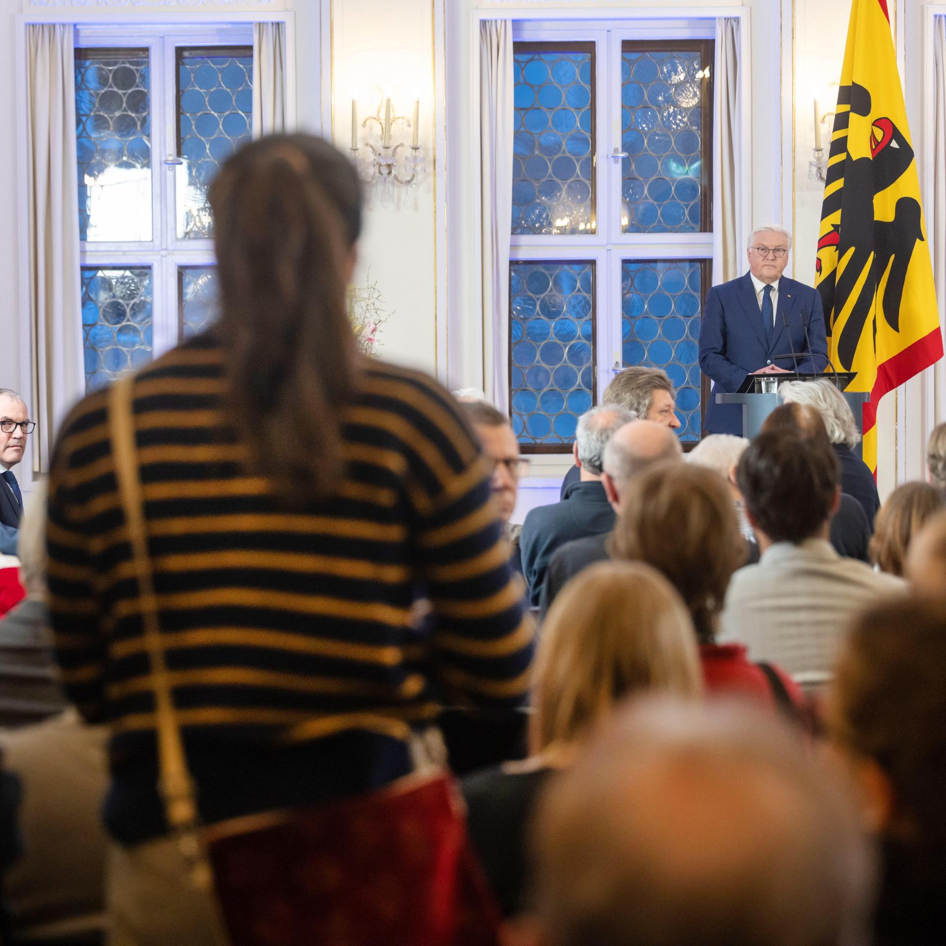 Zwei Frauen stehen in den Zuschauerrängen und stören die Rede von Bundespräsident Frank-Walter Steinmeier auf der Leipziger Buchmesse mit Rufen. Im Hintergrund ist Steinmeier zu sehen, wie er an einem Rednerpult steht und neben ihm steht die Bundeswappenfahne, also die Deutschlandfahne mit Adler. 