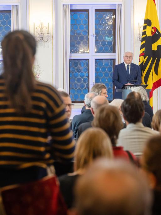 Zwei Frauen stehen in den Zuschauerrängen und stören die Rede von Bundespräsident Frank-Walter Steinmeier auf der Leipziger Buchmesse mit Rufen. Im Hintergrund ist Steinmeier zu sehen, wie er an einem Rednerpult steht und neben ihm steht die Bundeswappenfahne, also die Deutschlandfahne mit Adler. 