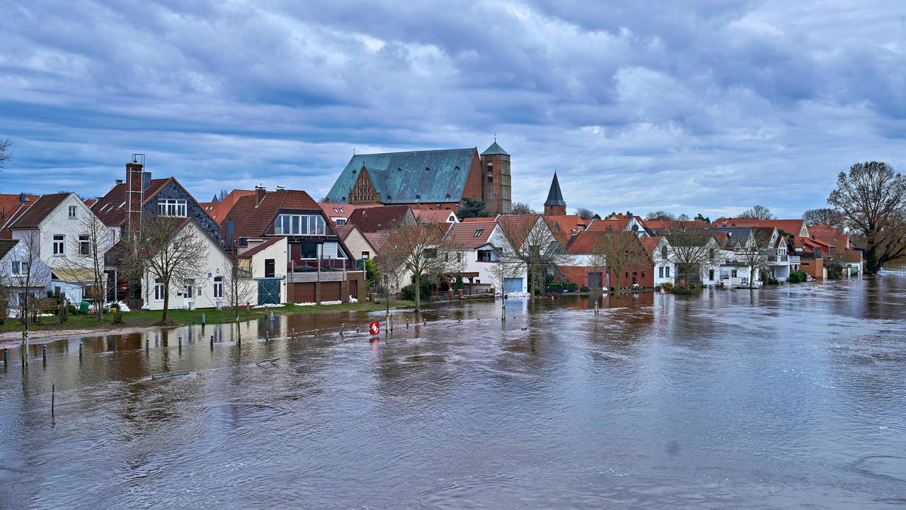 Panorama der Stadt Verden in Niedersachsen. Im Vordergrund überschwemmtes Gebiet, zwischen den Häusern kann man eine Kirche sehen. Die Wolken hängen Dunkel über den Dächern.